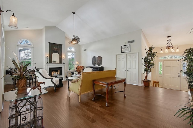 living room with wood finished floors, visible vents, a glass covered fireplace, high vaulted ceiling, and a notable chandelier