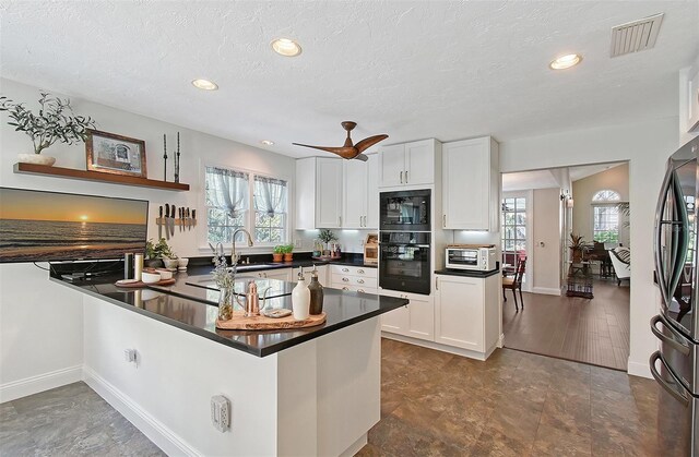 kitchen featuring dark countertops, visible vents, a sink, black appliances, and white cabinetry