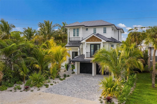 coastal home with a standing seam roof, metal roof, stairs, french doors, and driveway