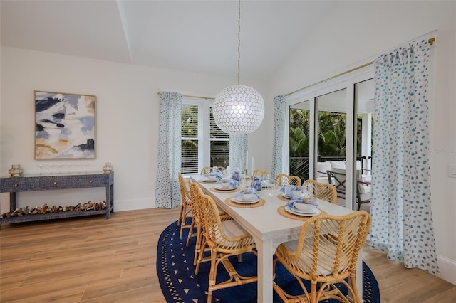 dining space with light wood finished floors, a notable chandelier, baseboards, and vaulted ceiling