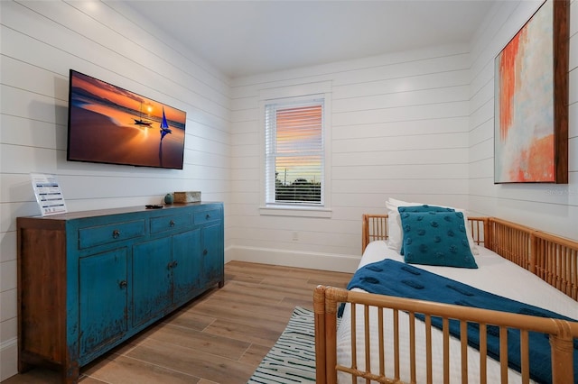 bedroom with wood walls, baseboards, and wood finished floors