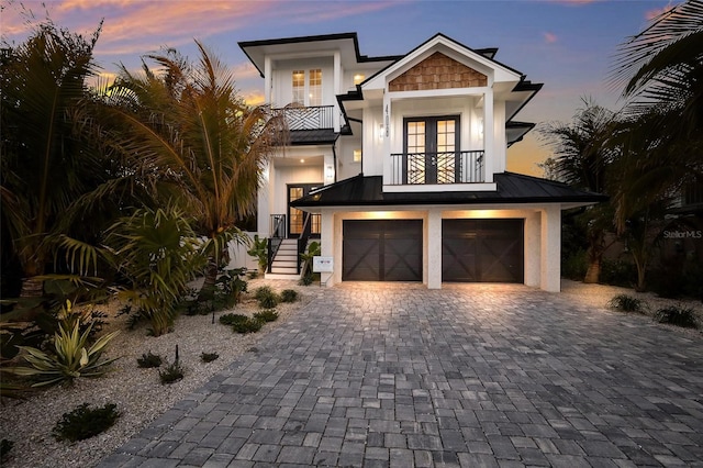 view of front of property with an attached garage, decorative driveway, a balcony, stucco siding, and a standing seam roof