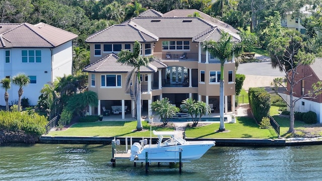 back of house with a water view, stucco siding, a balcony, and a tile roof