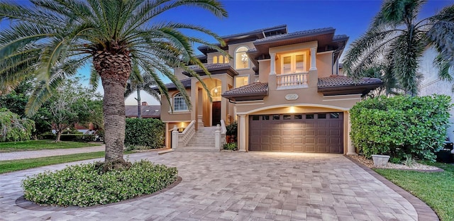 mediterranean / spanish house featuring a tiled roof, a garage, decorative driveway, a balcony, and stucco siding
