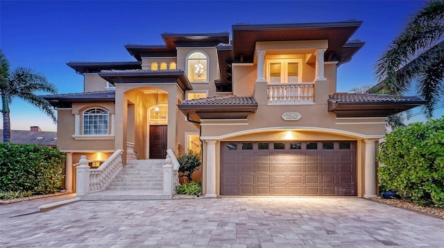 mediterranean / spanish-style home featuring a tiled roof, decorative driveway, a balcony, an attached garage, and stucco siding