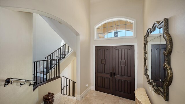 foyer entrance featuring arched walkways, a high ceiling, baseboards, and stairs