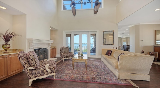 living room featuring french doors, a fireplace with raised hearth, dark wood finished floors, and a towering ceiling