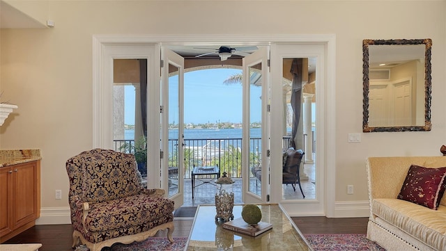 living area featuring baseboards, dark wood-style flooring, a water view, and ceiling fan