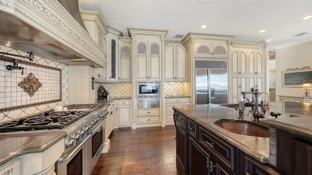 kitchen featuring visible vents, built in appliances, premium range hood, cream cabinets, and a warming drawer