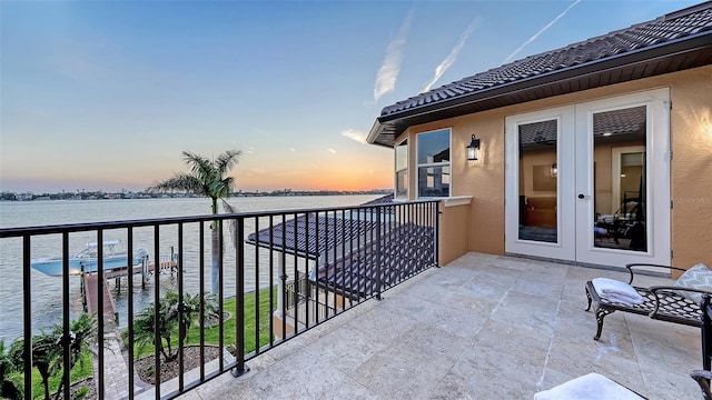 balcony at dusk with a water view and french doors
