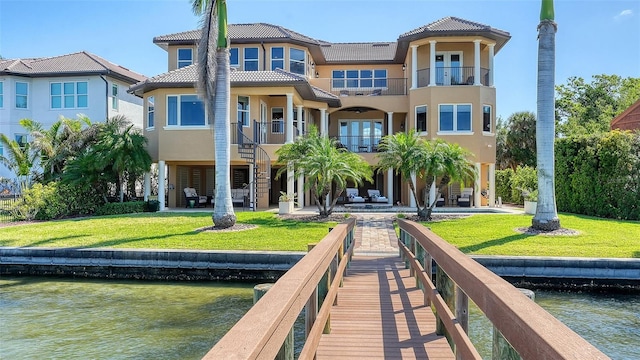 rear view of house featuring a tile roof, a balcony, a yard, a water view, and stucco siding