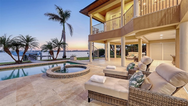 patio terrace at dusk with a water view, outdoor lounge area, a pool with connected hot tub, and a balcony