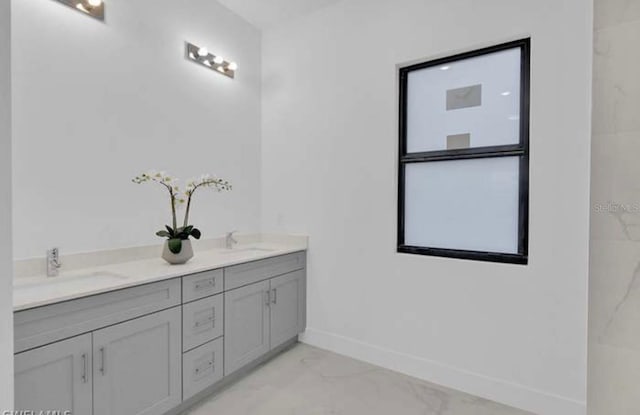 full bath featuring double vanity, baseboards, marble finish floor, and a sink