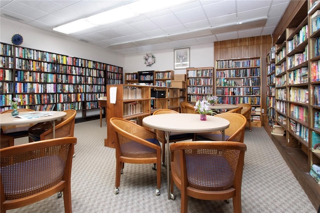 living area with wall of books, carpet, and a paneled ceiling