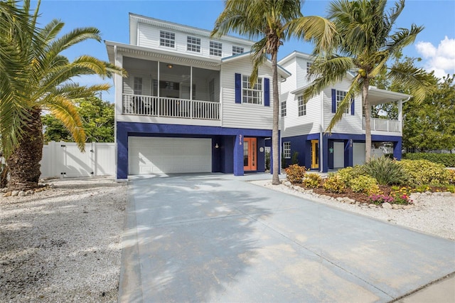 coastal home with a gate, driveway, an attached garage, fence, and stucco siding