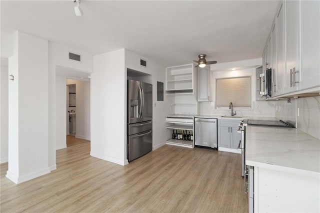 kitchen with ceiling fan, decorative backsplash, appliances with stainless steel finishes, a sink, and light wood finished floors