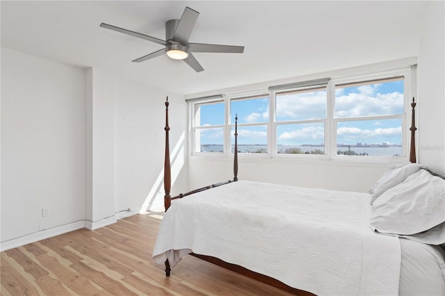 bedroom featuring a water view, baseboards, light wood finished floors, and ceiling fan