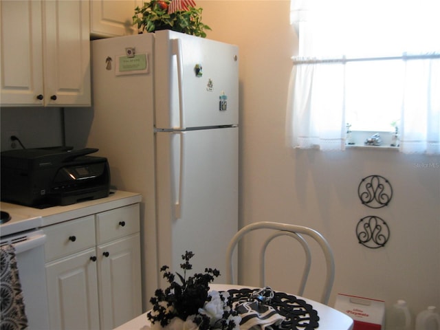 kitchen with freestanding refrigerator, light countertops, and white cabinetry