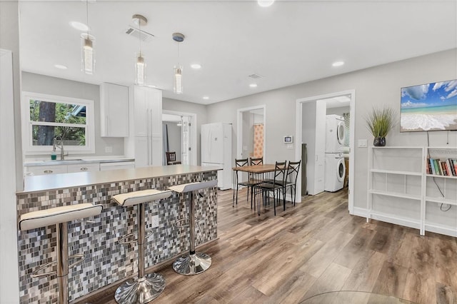 kitchen featuring a sink, stacked washer / drying machine, light wood-style flooring, white cabinetry, and visible vents