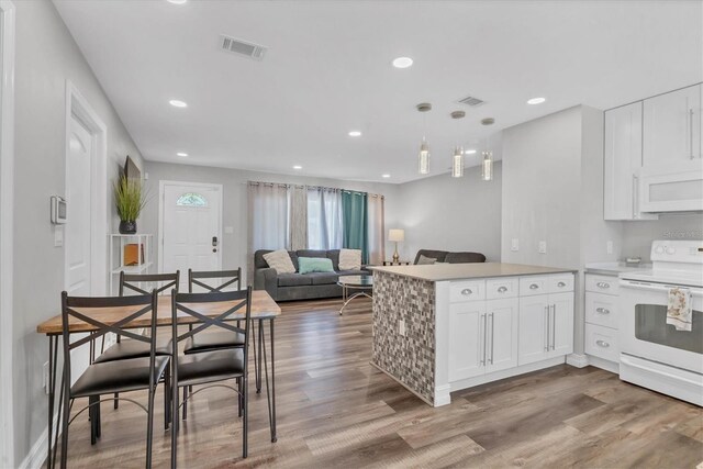 kitchen featuring wood finished floors, visible vents, white appliances, a peninsula, and white cabinetry