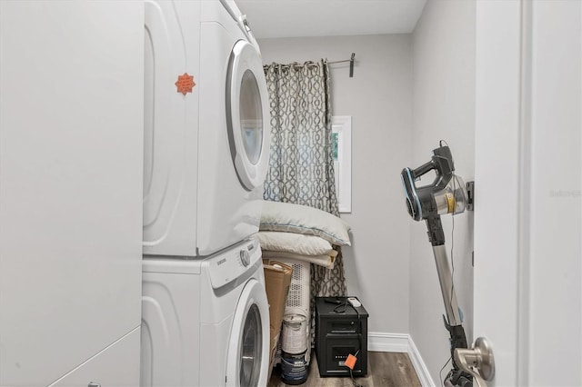 laundry room featuring stacked washer / drying machine, baseboards, wood finished floors, and laundry area