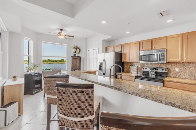 7803 Grand Estuary Trl Unit 102, Bradenton, FL 34212 - kitchen with tasteful backsplash, light brown cabinetry, a ceiling fan, appliances with stainless steel finishes, and light tile patterned flooring