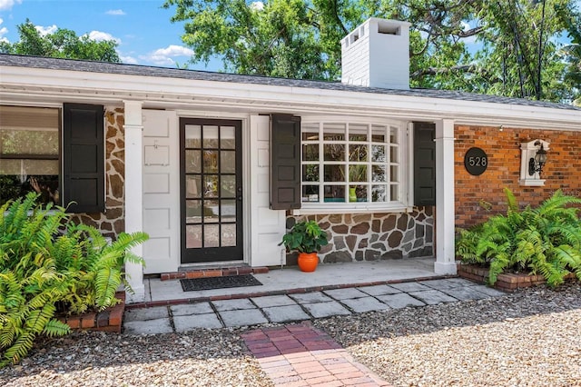 view of exterior entry with stone siding, a chimney, and covered porch