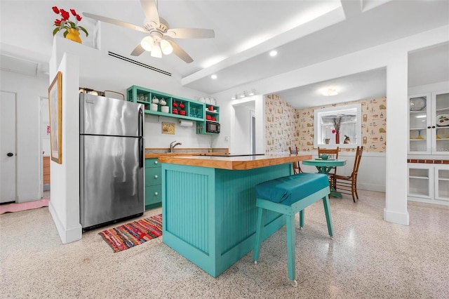 kitchen with light speckled floor, freestanding refrigerator, a ceiling fan, butcher block counters, and a breakfast bar