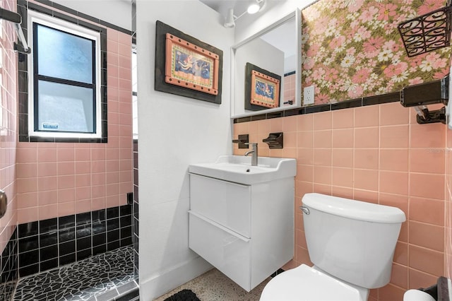 full bath featuring wallpapered walls, a tile shower, toilet, vanity, and wainscoting