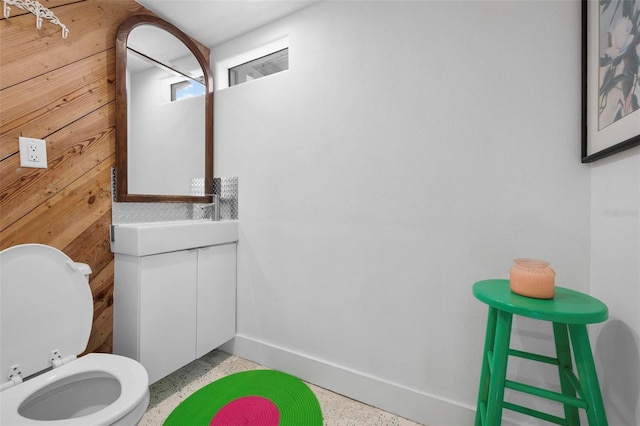half bath featuring speckled floor, vanity, toilet, and baseboards
