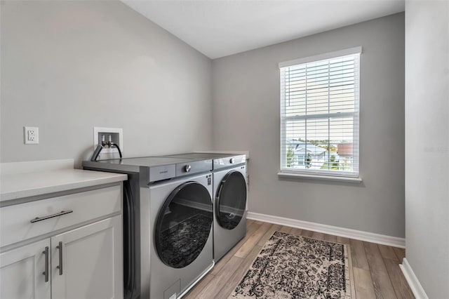 clothes washing area featuring washing machine and clothes dryer, a healthy amount of sunlight, light wood finished floors, and cabinet space