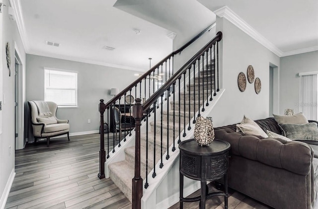staircase featuring baseboards, ornamental molding, wood finished floors, and visible vents