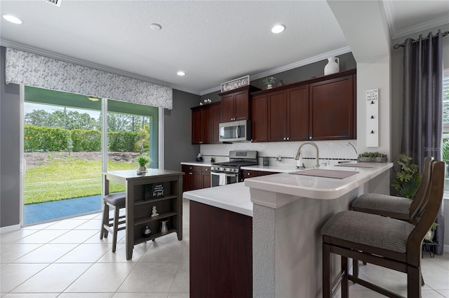 kitchen featuring light countertops, backsplash, crown molding, a kitchen bar, and appliances with stainless steel finishes