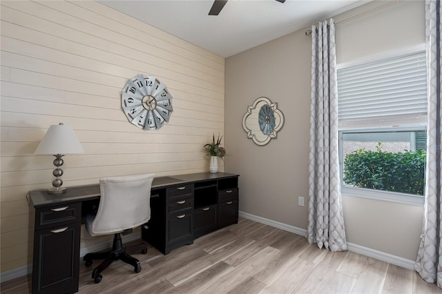 home office featuring ceiling fan, baseboards, wooden walls, and light wood-style flooring