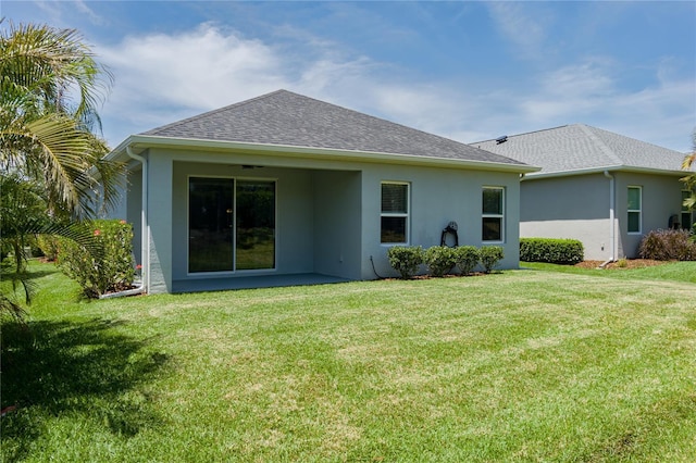 rear view of property featuring stucco siding, a shingled roof, and a lawn