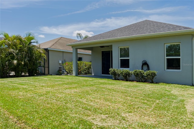 view of front of home featuring ceiling fan, roof with shingles, a front yard, and stucco siding