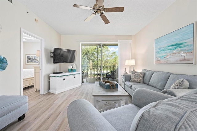 living area with ceiling fan, light wood finished floors, a textured ceiling, baseboards, and visible vents