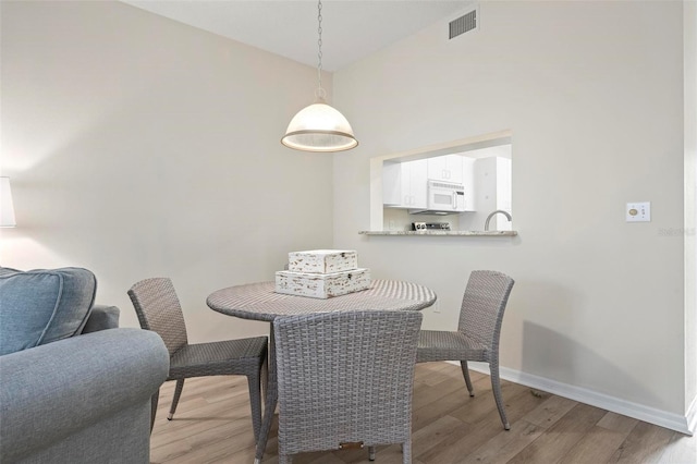 dining room featuring baseboards, visible vents, light wood finished floors, and a towering ceiling