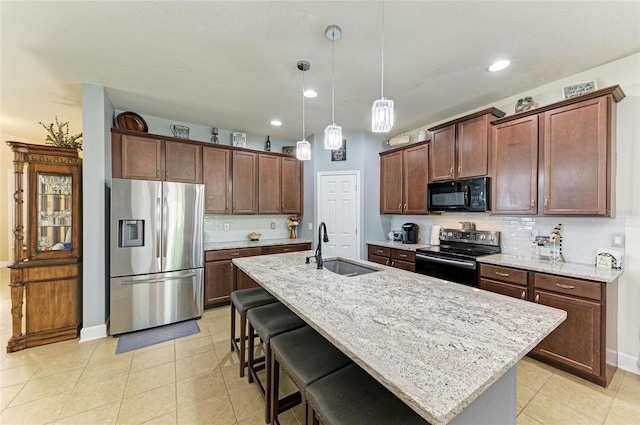 kitchen featuring a kitchen island with sink, tasteful backsplash, light stone counters, a sink, and appliances with stainless steel finishes