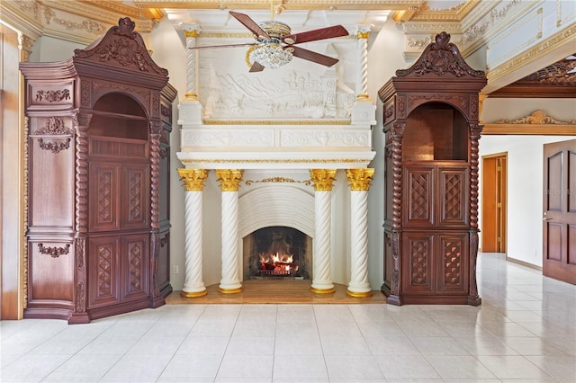 living area featuring a lit fireplace, baseboards, ornamental molding, tile patterned floors, and a ceiling fan