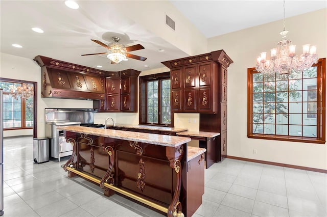 kitchen featuring a kitchen island with sink, custom range hood, ceiling fan with notable chandelier, baseboards, and pendant lighting
