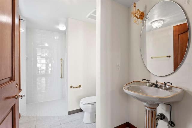 bathroom with toilet, tile patterned flooring, and tiled shower