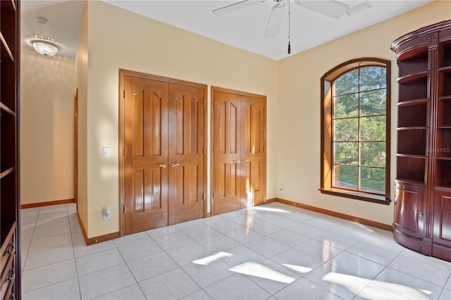 unfurnished bedroom with light tile patterned floors, visible vents, two closets, and baseboards