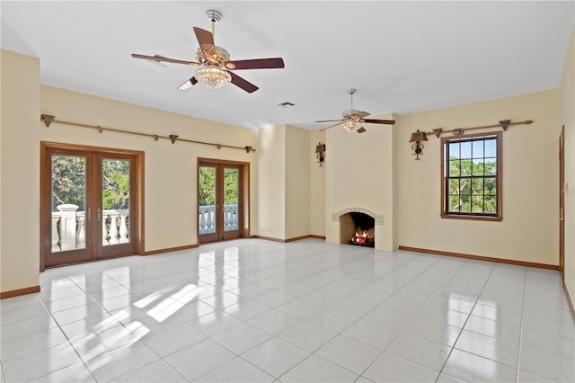 unfurnished living room with ceiling fan, french doors, a healthy amount of sunlight, and a lit fireplace