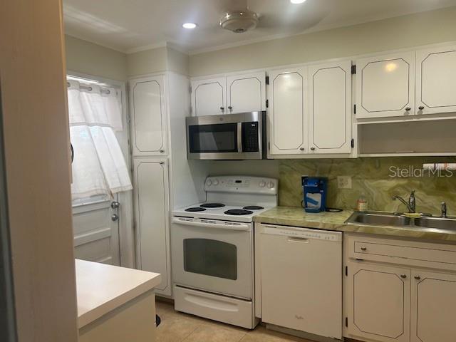 7461 W Country Club Dr N Unit 201, Sarasota, FL 34243 - kitchen featuring white appliances, a sink, ornamental molding, white cabinets, and light countertops
