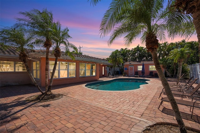 pool at dusk with a patio area, an outdoor pool, and fence