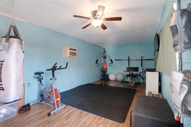 workout room with a ceiling fan, wood finished floors, and a wall unit AC