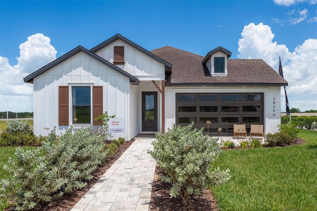 view of front of house with a garage, roof with shingles, board and batten siding, and a front lawn