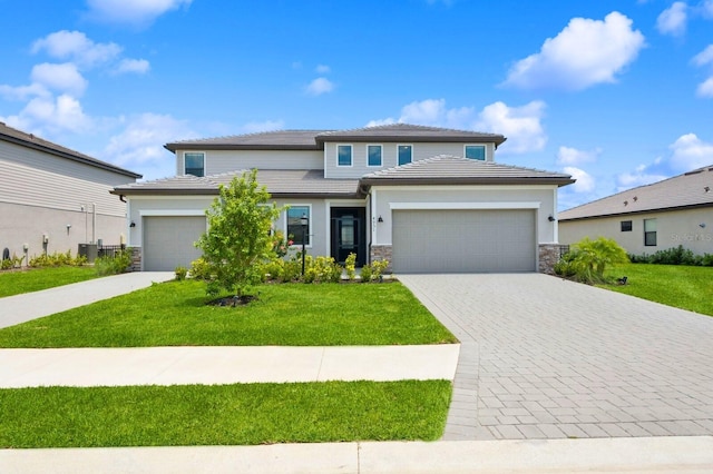 prairie-style house featuring stone siding, a garage, stucco siding, a front lawn, and decorative driveway
