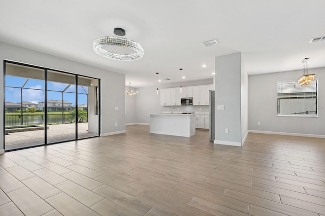 unfurnished living room with visible vents, baseboards, and an inviting chandelier